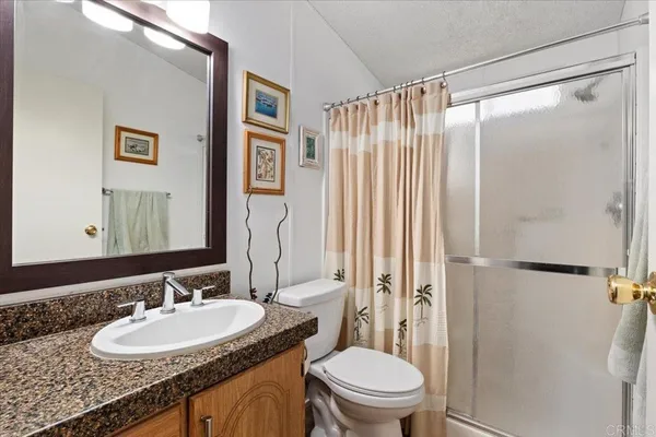 a bathroom with a granite countertop sink toilet a mirror a shower and a mirror