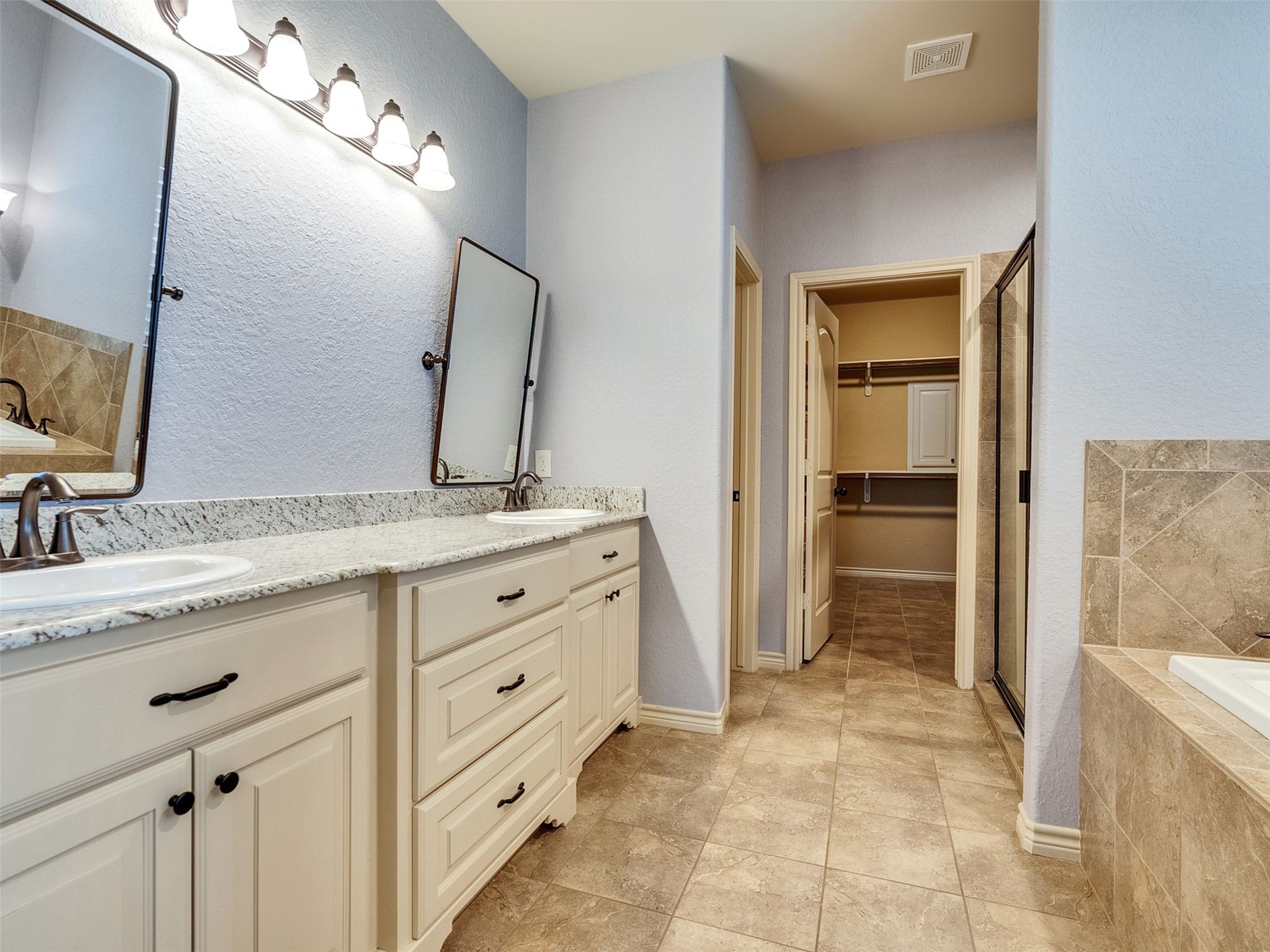 18005 Cindy Lane Conroe, TX 77302 - Photo 31 of 49 This spacious bathroom features a double vanity with granite countertops, elegant lighting, and ample storage. It includes a tiled shower, a bathtub, and leads to a generous walk-in closet.