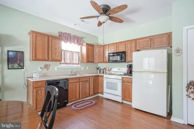 a kitchen with stainless steel appliances granite countertop a refrigerator a sink dishwasher a stove and white countertops with wooden floor