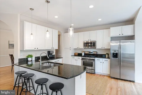 a kitchen with stainless steel appliances granite countertop a stove a refrigerator a kitchen island a dining table and chairs with wooden floor
