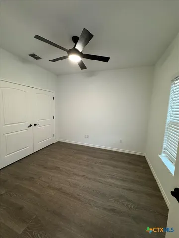 an empty room with wooden floor fan and windows