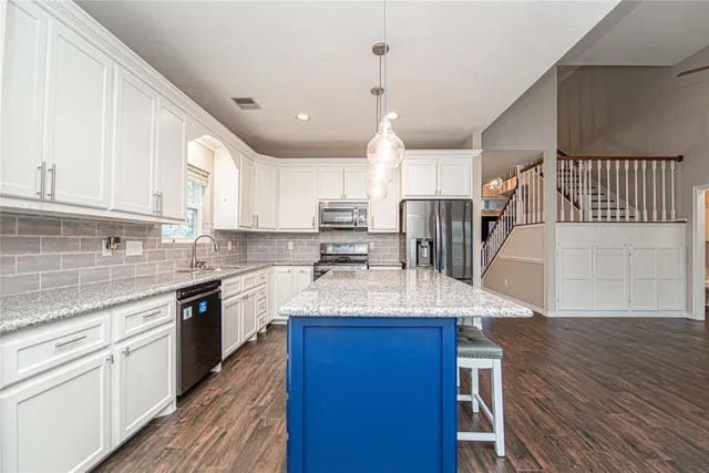 a kitchen with stainless steel appliances granite countertop a sink dishwasher a stove and white cabinets with wooden floor