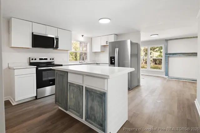 a kitchen with stainless steel appliances a stove a sink a microwave a refrigerator a stove and white cabinets with wooden floor