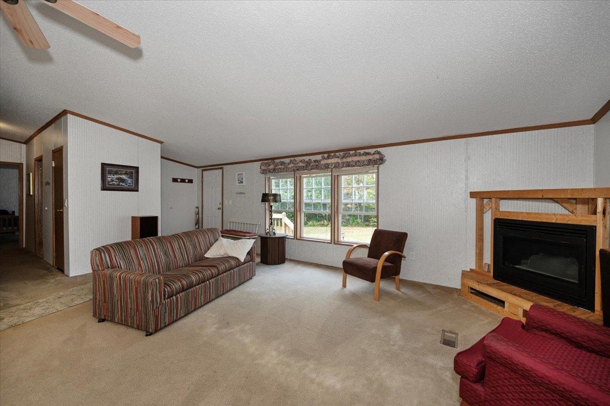 11032 South Ellen Smith Road Solon Springs, WI 54873 - Photo 8 of 33 Carpeted living area featuring a fireplace with raised hearth, ornamental molding, a textured ceiling, and vaulted ceiling