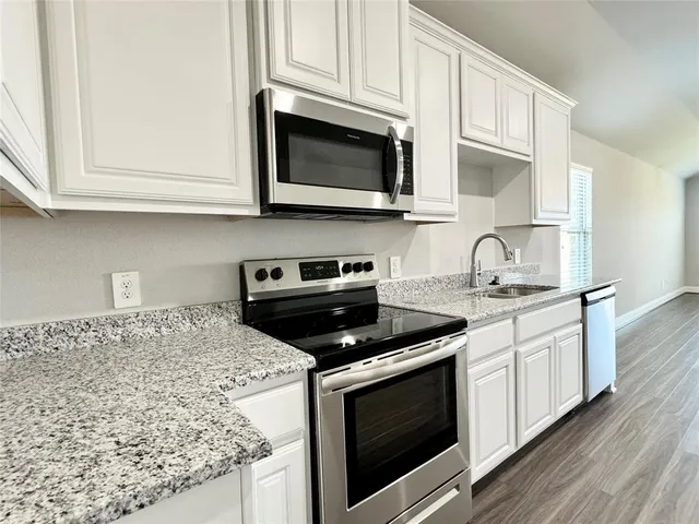 a kitchen with stainless steel appliances granite countertop white cabinets and a stove a oven with wooden floor