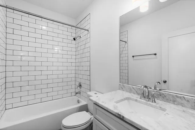 a bathroom with a granite countertop bathtub shower sink vanity and toilet