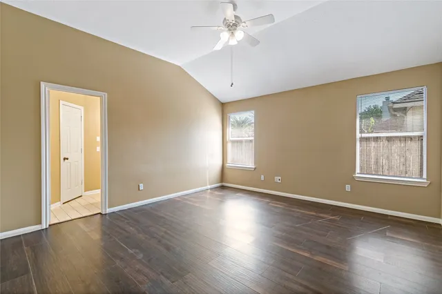 an empty room with wooden floor chandelier fan and windows