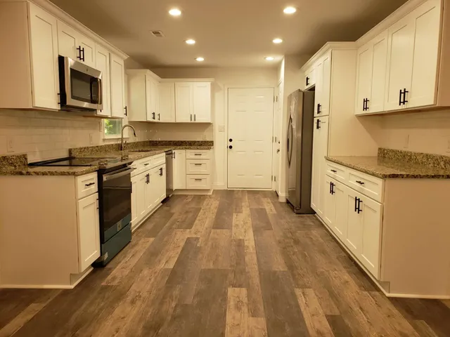a large kitchen with stainless steel appliances granite countertop a stove a sink and white cabinets