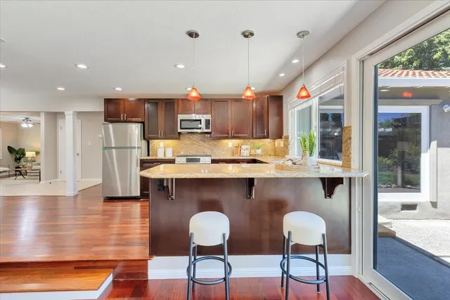 a kitchen with stainless steel appliances kitchen island granite countertop a table chairs in it and wooden floors