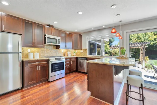 a kitchen with kitchen island granite countertop wooden floors stainless steel appliances and a refrigerator