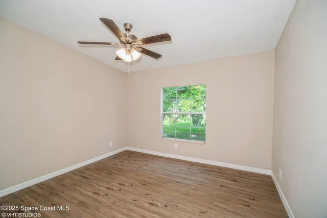 an empty room with wooden floor fan and windows
