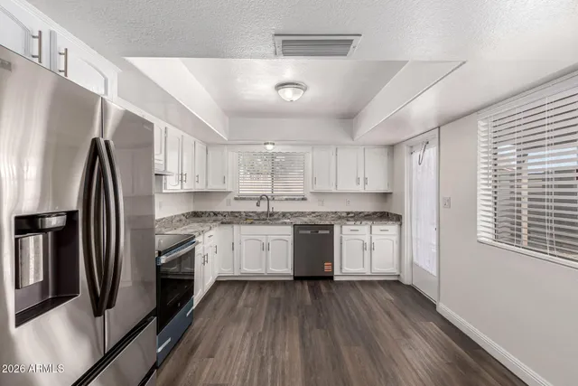 a kitchen with stainless steel appliances granite countertop a refrigerator a sink dishwasher a stove and white countertops with wooden floor