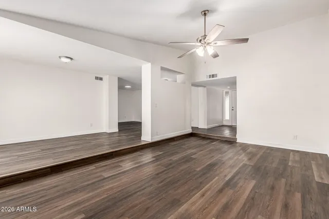 a view of an empty room with wooden floor and a ceiling fan