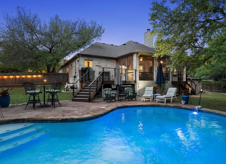 15208 Nightingale Lane Austin, TX 78734 - Photo 35 of 40 Back of property at dusk with a patio area, stone siding, a sunroom, a chimney, and a fenced backyard