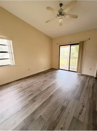 an empty room with wooden floor ceiling fan and windows