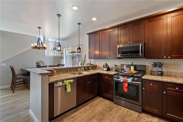 a kitchen with stainless steel appliances granite countertop a stove a sink dishwasher a microwave oven and a refrigerator with wooden cabinets