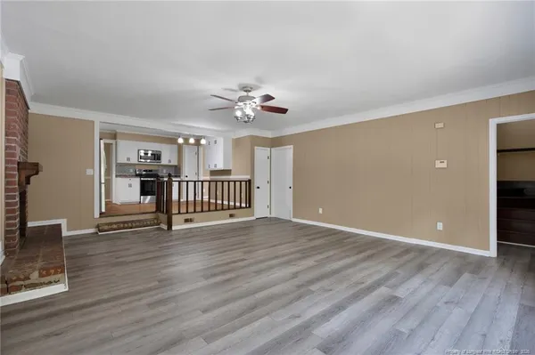 a view of an empty room with wooden floor and a ceiling fan