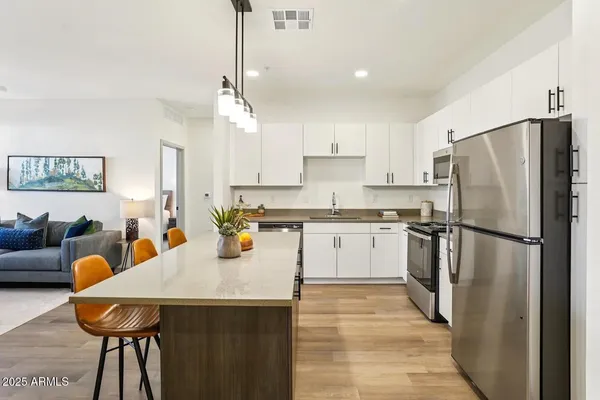 a kitchen with stainless steel appliances a refrigerator a stove a sink dishwasher a dining table and chairs with wooden floor