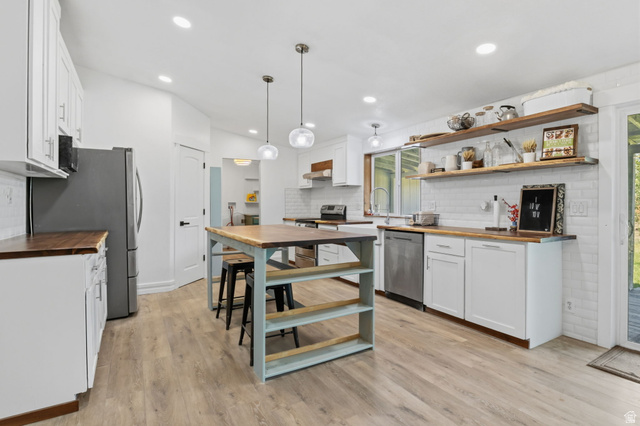 4270 River Road Oakley, UT 84055 - Photo 14 of 46 Open-concept kitchen featuring wood-finish flooring, white cabinetry, wood countertops, a central island with bar seating, and stainless steel appliances
