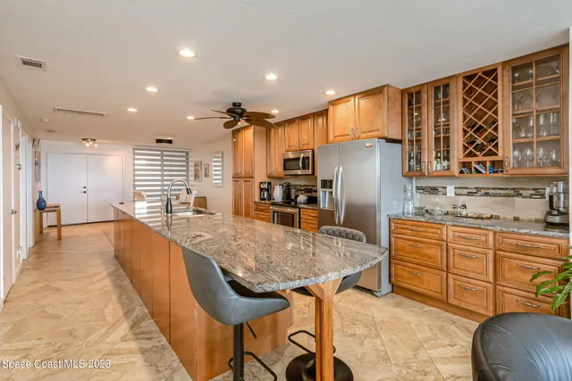 a kitchen with stainless steel appliances granite countertop a kitchen island a stove a refrigerator a sink a dining table and chairs with wooden floor