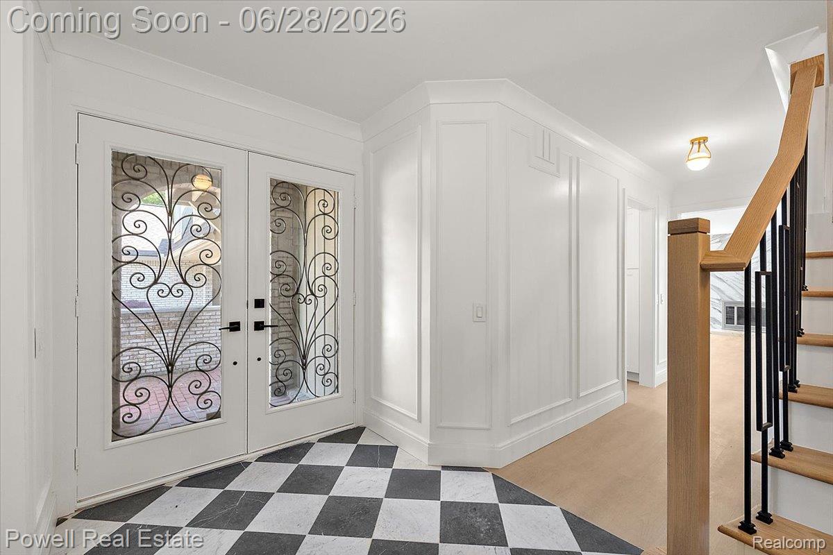 1447 Ravineview Court, Unit C12 Bloomfield Hills, MI 48304 - Photo 10 of 49 Foyer with checkerboard tile flooring, double entry doors featuring decorative ironwork, paneled wall detailing, and a staircase with a natural wood handrail and black balusters