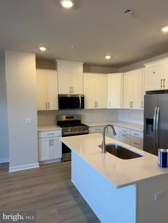 a kitchen with stainless steel appliances granite countertop a sink a stove a refrigerator a microwave oven with white cabinets and wooden floor