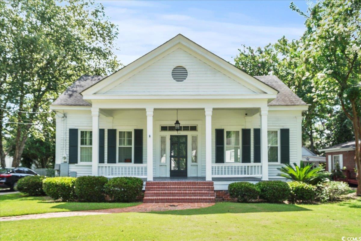 Greek revival inspired property with a front yard, covered porch, and a shingled roof