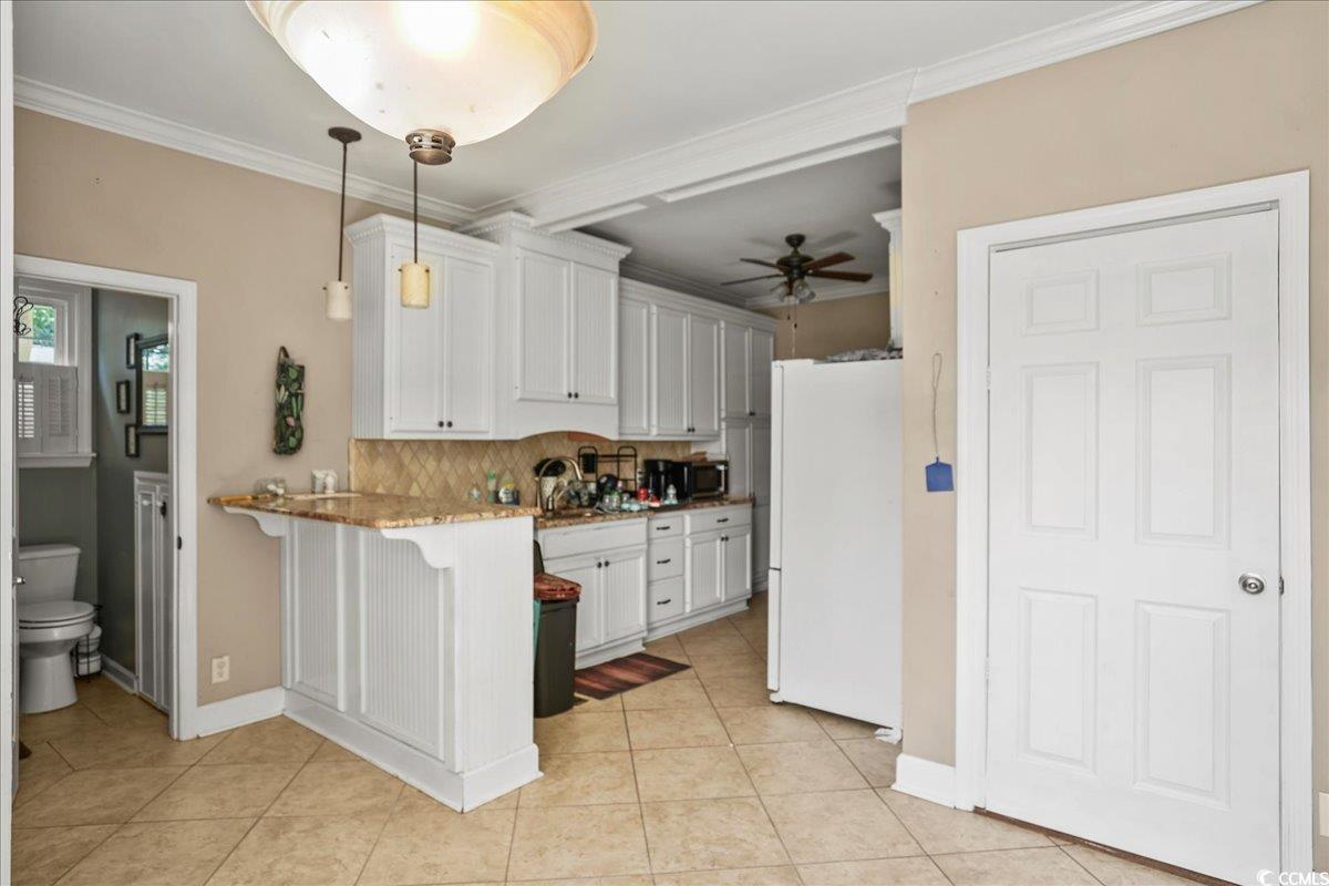 818 Evans Road Marion, SC 29571 - Photo 15 of 39 Kitchen with freestanding refrigerator, white cabinetry, a kitchen bar, a peninsula, and ornamental molding