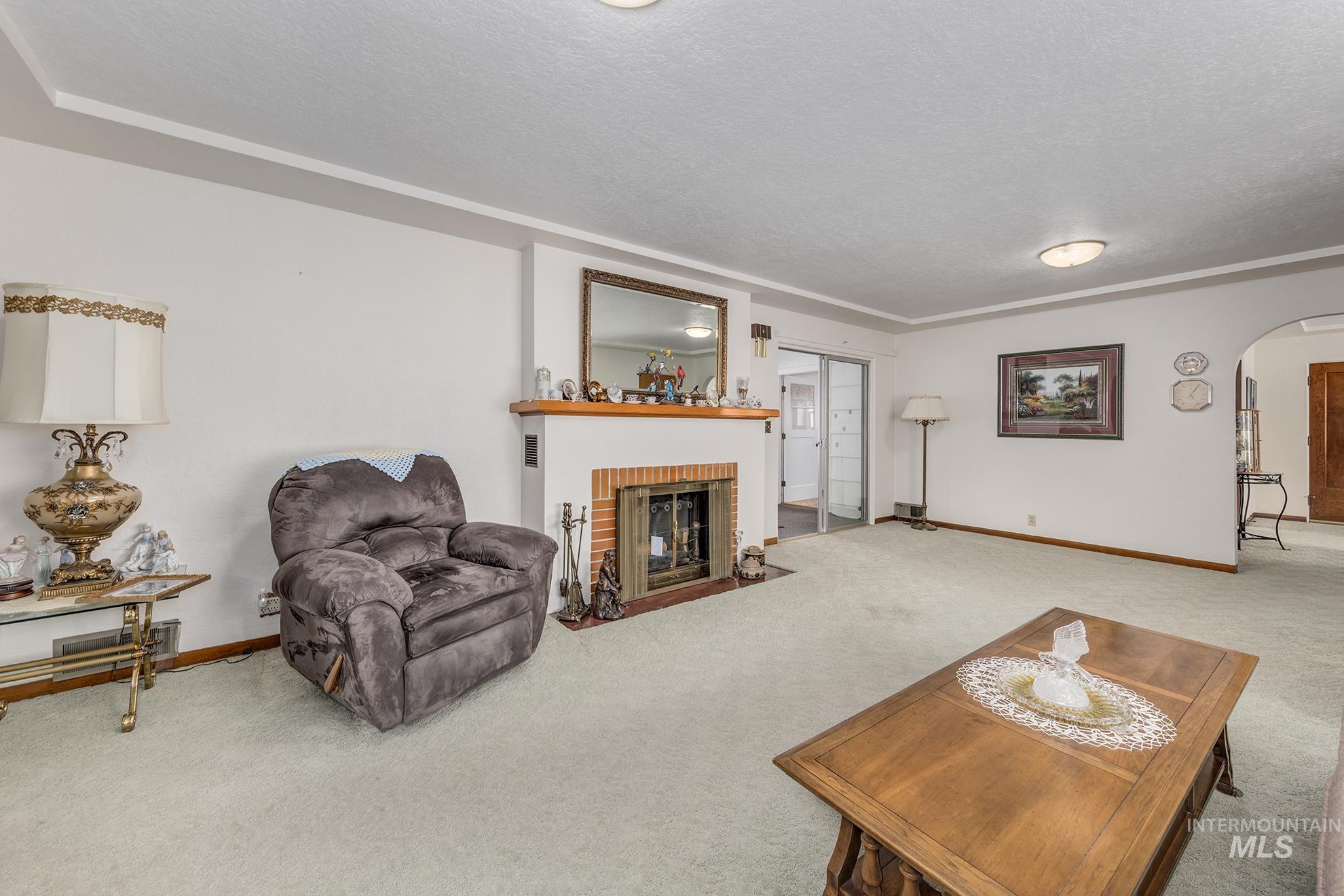116 Pioneer Road Weiser, ID 83672 - Photo 6 of 45 Living area featuring arched walkways, carpet, a textured ceiling, and a brick fireplace