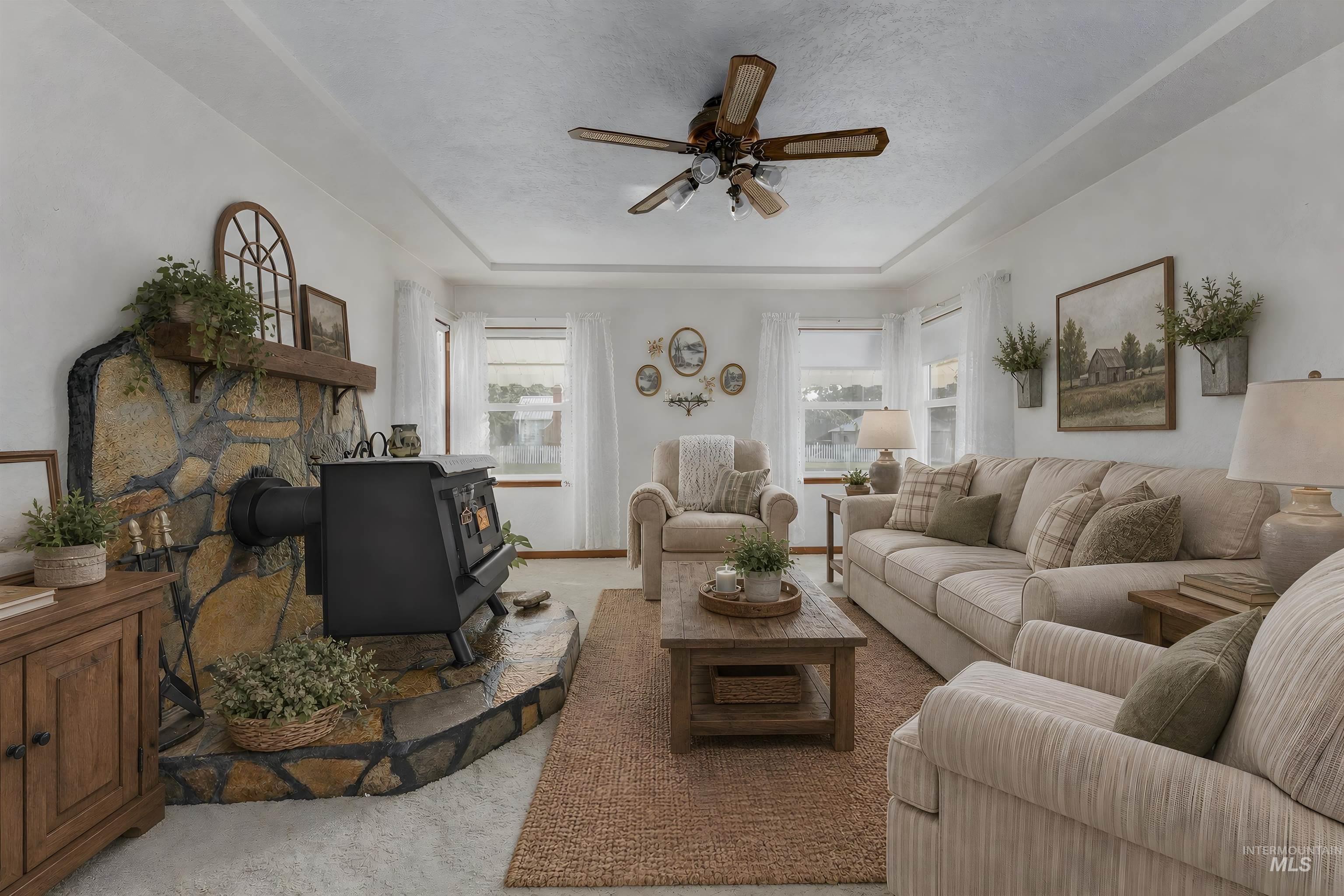 116 Pioneer Road Weiser, ID 83672 - Photo 8 of 45 Living area featuring a stone wood-burning stove with mantel, tray ceiling, and ceiling fan