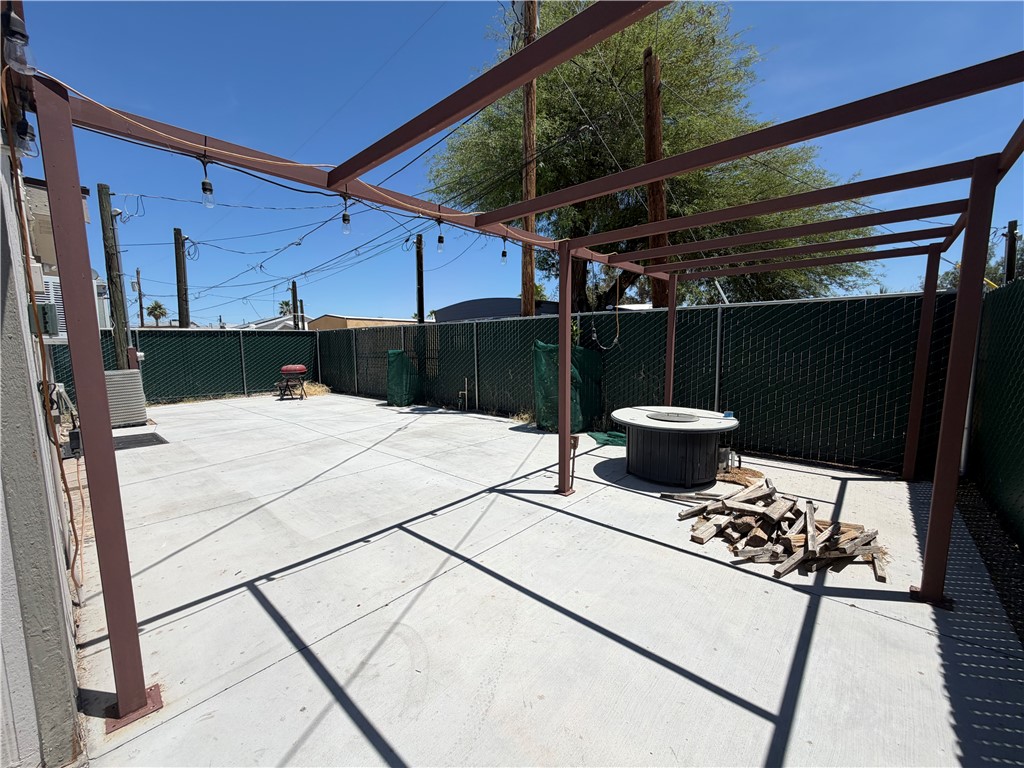 1910 Rio Grande Road Bullhead City, AZ 86442 - Photo 28 of 29 Spacious concrete patio featuring a metal pergola structure, string lighting, and full chain-link fencing with privacy slats