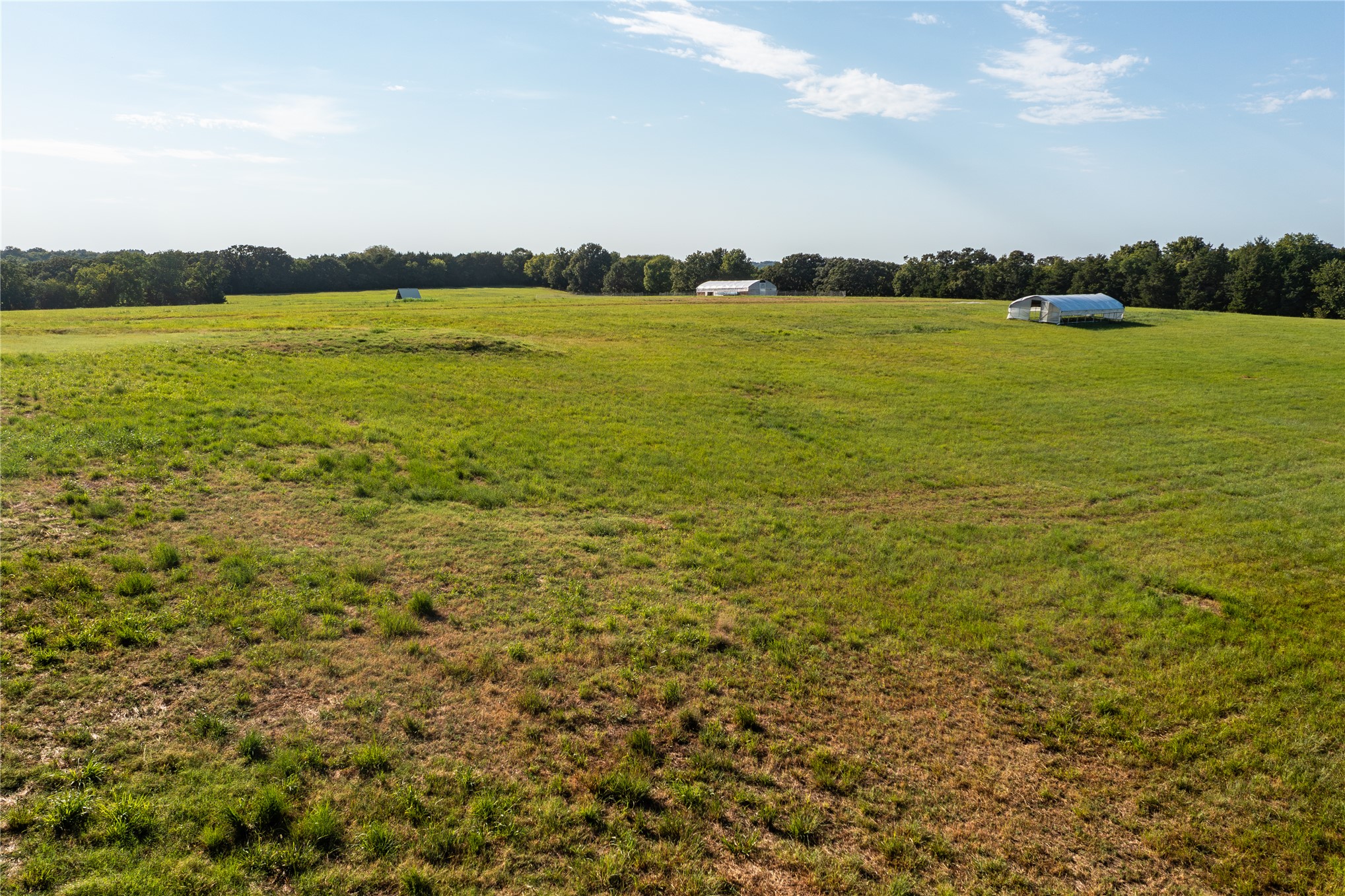 0 West Dunkin Road Cushing, OK 74023 - Photo 2 of 62 Expansive open field with green grass, bordered by a treeline in the distance, featuring two white agricultural structures