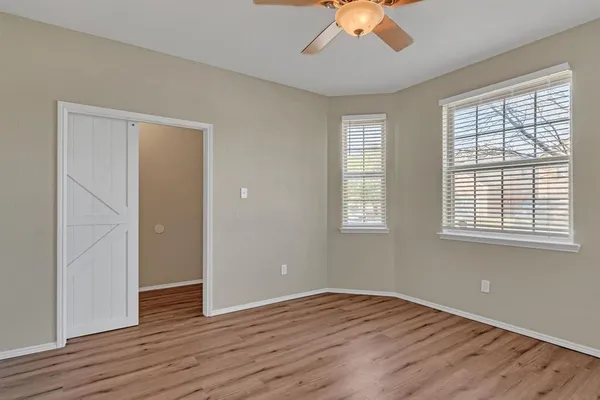 an empty room with wooden floor chandelier fan and windows