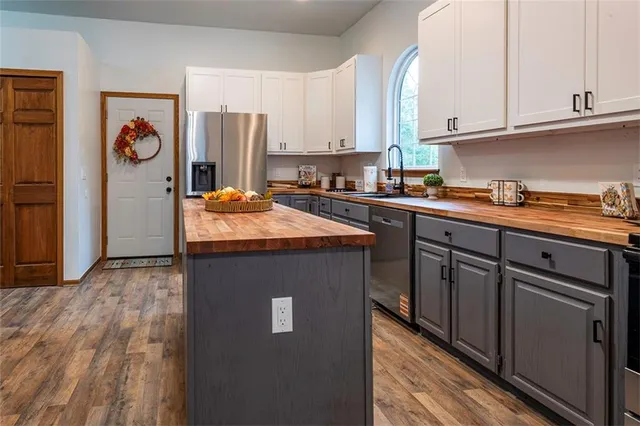 a kitchen with stainless steel appliances granite countertop a refrigerator a sink dishwasher and white cabinets with wooden floor