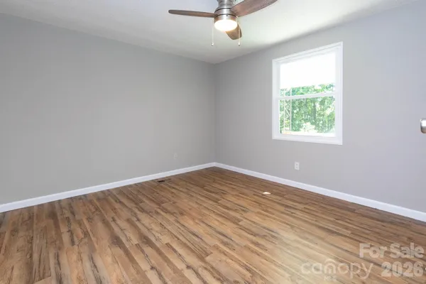 an empty room with wooden floor chandelier fan and windows