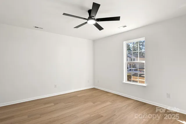 a view of a livingroom with a hardwood floor a ceiling fan and windows