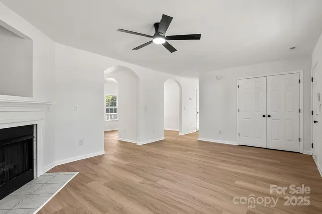 a view of an empty room with wooden floor a fireplace and a window