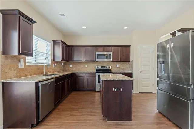 a kitchen with stainless steel appliances granite countertop a refrigerator a sink dishwasher a stove top oven and a refrigerator