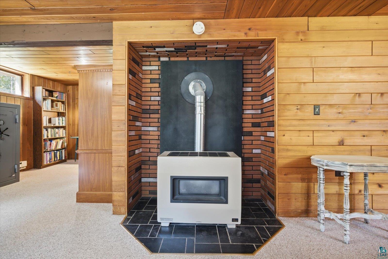 6377 Bergstrom Road Saginaw, MN 55779 - Photo 18 of 20 Wood-paneled room featuring a built-in white stove within a brick hearth, set on a black tile floor surround