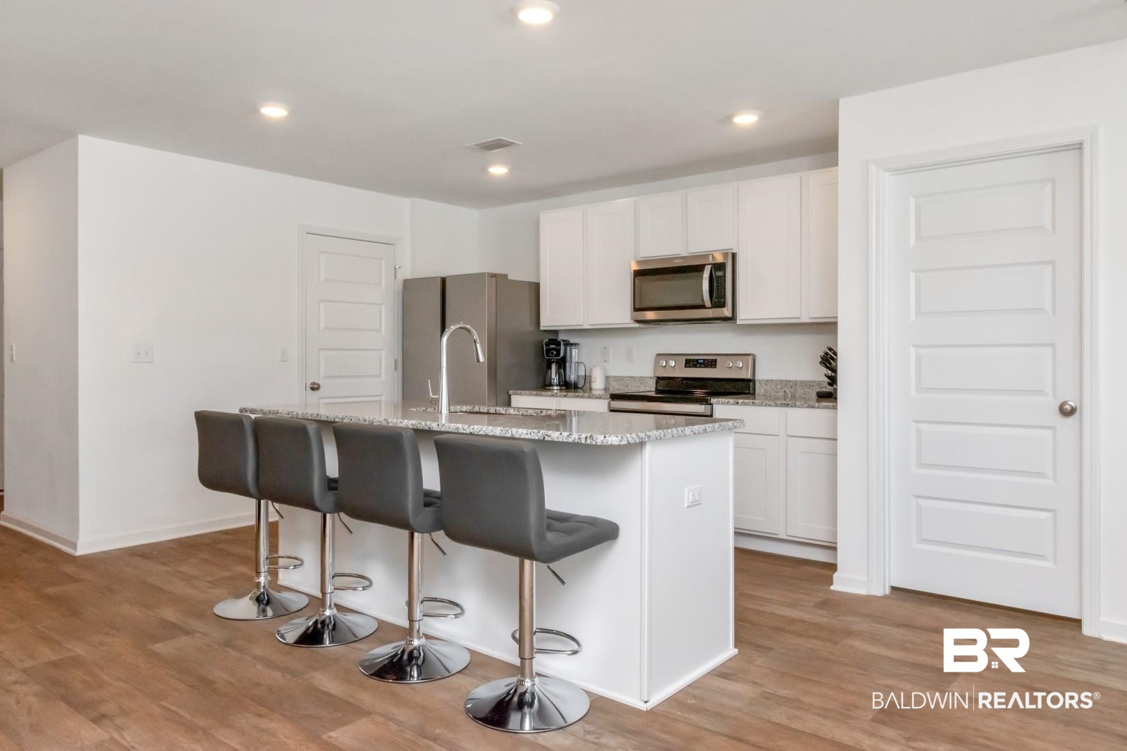 10921 Northern Dancer Court Daphne, AL 36526 - Photo 14 of 32 Kitchen with a kitchen bar, light wood-type flooring, white cabinetry, stainless steel appliances, and a kitchen island with sink