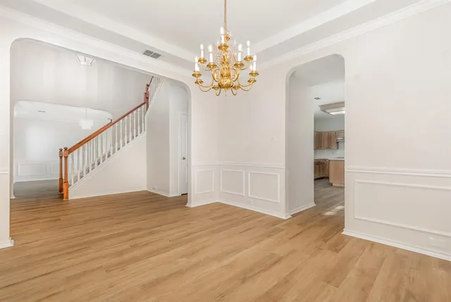 a view of an empty room with chandelier and wooden floor