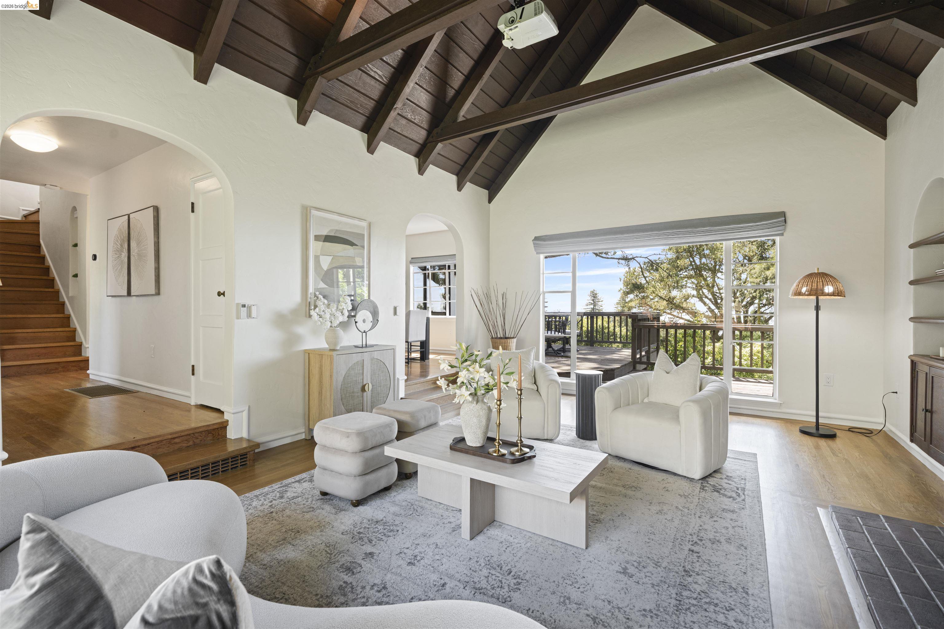 Living area featuring a vaulted wood-beam ceiling, full-height windows, a wooden balcony, hardwood flooring, and arched doorways