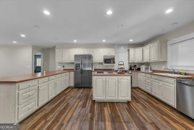 a large white kitchen with kitchen island a stove a sink a refrigerator and white cabinets with wooden floor