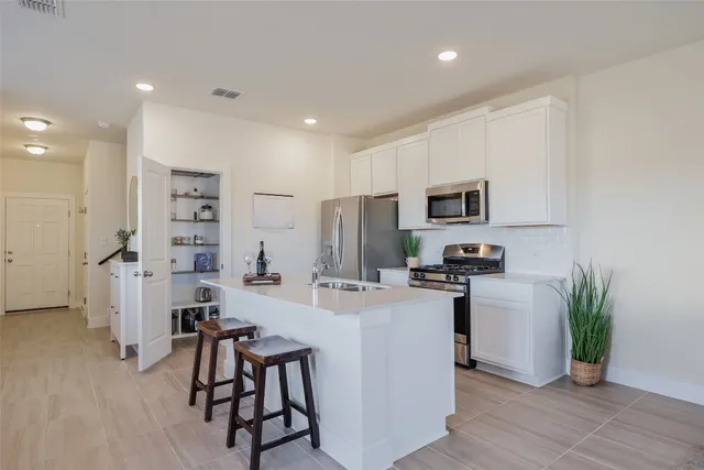 a kitchen with stainless steel appliances a microwave a stove a refrigerator a sink a dining table and chairs with wooden floor