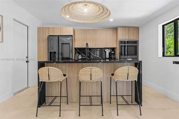 a kitchen with stainless steel appliances kitchen island granite countertop a dining table chairs and a refrigerator