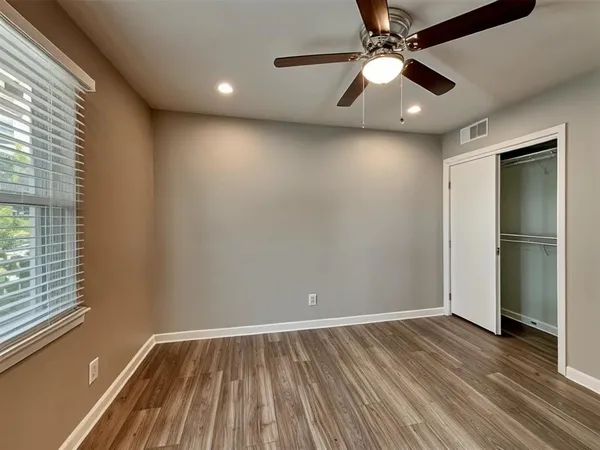 an empty room with wooden floor fan and windows