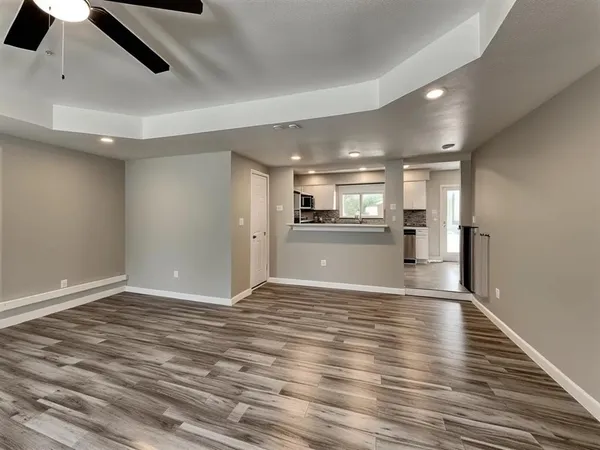 an empty room with wooden floor kitchen view and windows