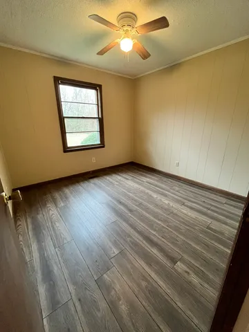 an empty room with wooden floor chandelier fan and windows