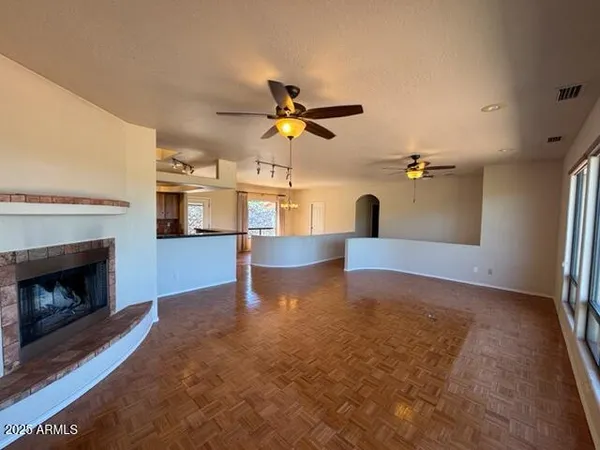 a view of a livingroom with fireplace a ceiling fan and a kitchen view
