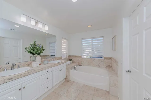 a spacious bathroom with a granite countertop double vanity sink a bathtub and mirror